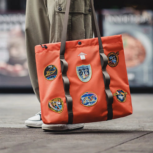 Orange tote bag with patches held by a person on a blurred street background